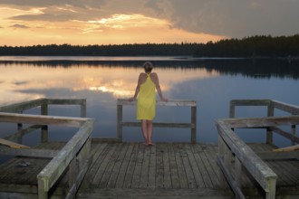 Young woman standing on a pier and admired the sunset on a lake in Småland, Sweden, Europe