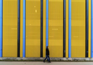 Pedestrian woman walking in front of a colorful Industrial background with straight patterned