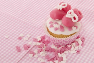 Pink cupcake with baby shoes and hearts