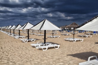 Different parasols and sun loungers on the empty beach on Tavira island before storm, Algarve.