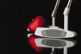 Two different golf putters and red heart on a black glass desk