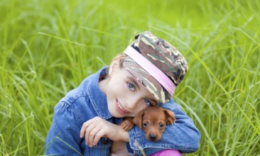Little girl with pet puppy mascot mini pinscher in outdoor green grass
