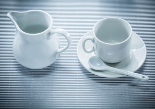 White ceramic cup saucer teaspoon creamer on striped background