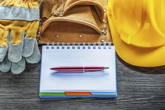 Notepad pen tool belt safety gloves hard hat on wooden board