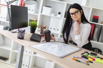 A young girl with glasses, wearing a white blouse and black trousers, works in the office. The girl