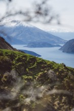 Green hills and snow-covered mountain with lake in the background under a clear sky, Roys Peak,