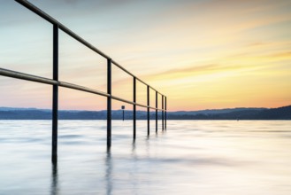 Railing in the lake at sunrise with gentle waves and peaceful sky, lido, Litzelstetten, Lake