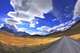 Gray dirt road in the Chile National Park Torres del Paine. Incredible shaped cloud formed by