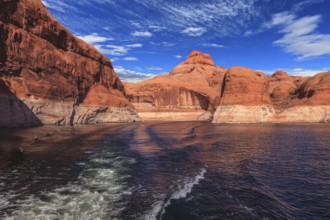 The foamy trace from powerboat crosses emerald waters. Hills from red sandstone surround the lake.