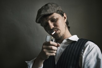 Young guy lights a cigarette, blows smoke, dressed in a retro style, in a beret, cinematic shot,