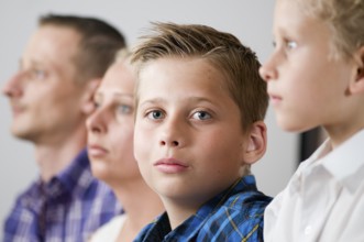 Close-up of a seven-year-old male teenager with parents lined up in the blurred background and