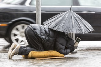 Homeless beggar is begging for money in a main street in Sofia holding an umbrella in a rainy day.