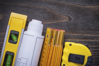 Roll of blueprints construction level tape-line and wooden meter on vintage wood board maintenance