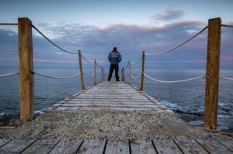 Person standing at the edge of a wooden pier in the sea at sunrise, People active outdoors enjoy