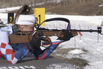 Sportswoman biathlete aiming, rifle shooting prone position. Biathlete Victoria Petrova Saint