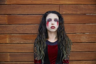 Halloween kid girl custome with bloody makeup on wooden wall