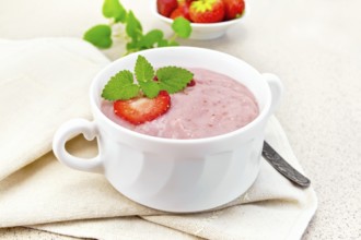 Strawberry soup with berries and mint in a bowl on a towel, spoon on a background of stone table