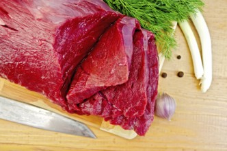 A piece of beef, garlic, peas pepper, dill, chives, knife on a wooden board