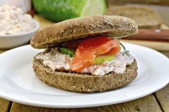 Sandwich of rye bread with cream, cucumber, dill and salmon on a plate on a wooden boards