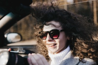 The woman with sunglasses and curly hair is cheerful, holding a camera in sunlight