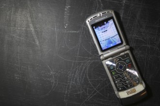 A Motorola flip phone open on a black textured surface showing the screen and keypad