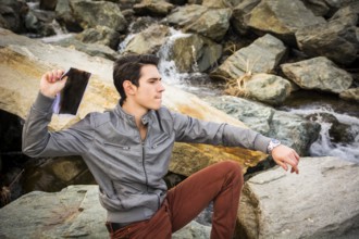 Handsome Young Man on Big Rocks at the River Throwing Something at the Distance
