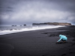 Photo of a person kneeling on a beautiful beach in Iceland, enjoying the mesmerizing view of the