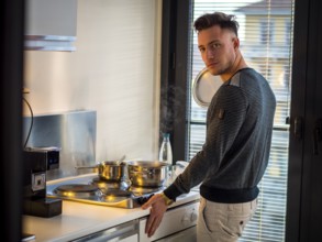 Handsome young man in his kitchen at home, cooking at the stove
