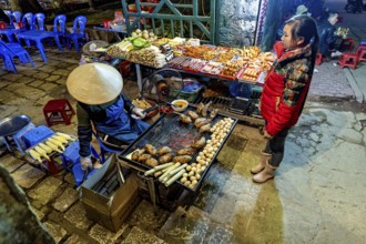 A busy street market with a stall selling grilled food surrounded by visitors, restaurant in the