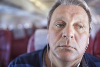Close-up shot of mature man listening to music in headphones during traveling by plane. He looking