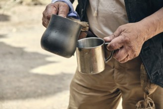 Hands of an adult man pouring hot coffee from a turk into a metal mug