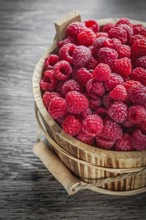Bucket with fresh raspberries on wooden board