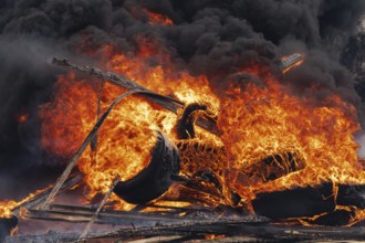 Burning cars wheels, strong flame of red-orange fire and clouds of black fumes in sky. Selective
