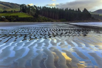 The sandy ripples of the beach reflect the clouds. Incredible sunset on the Pacific coast, New