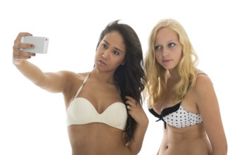 Black and white girl friends in bikini at the beach making selfie