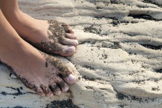 Unrecognised beautiful female food with beach sand on a white beach rocky surface