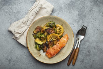 Delicious salmon fillet with grilled Brussels sprouts on plate, rustic stone background top view.