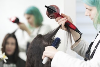 Female hairstylist dries brunette hair with red hair dryer and blue hairbrush in professional