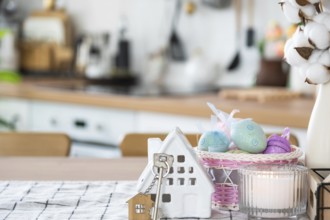Key and tiny house of cozy home with Easter decor with color eggs on table of kitchen. Building,
