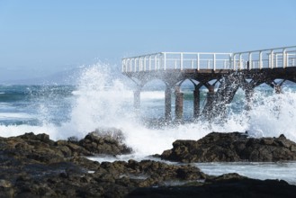 Waves breaking against pier on the beach of Corralejo at morning against blue sky