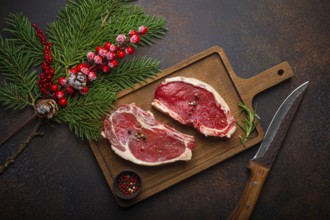 Two raw uncooked meat beef steaks on wooden cutting board with knife and seasonings on dark rustic