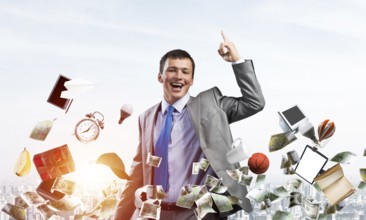 Young businessman and falling from sky various goods and cash. Handsome man in business suit and