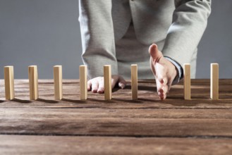 Businesswoman protecting dominoes from falling on wooden desk. Business assistance and leadership