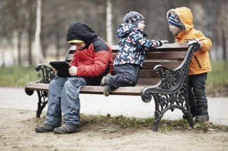Three young boys playing on a park bench in winter wrapped up warmly against the cold weather with