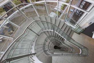 A modern spiral staircase with glass railings and a triangular shape in a bright room, Free and