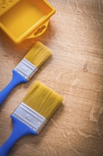 Two paintbrushes with blue handles and yellow paint can on wooden board construction concept