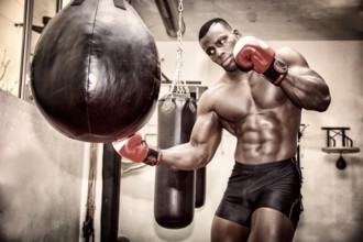 African black male boxer punching ball wearing boxing gloves in gym