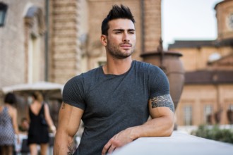 Attractaive muscular man with tattoo posing in European city center, Turin, Italy, looking at