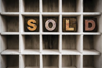 The word SOLD written in vintage ink stained wooden letterpress type in a partitioned printer's
