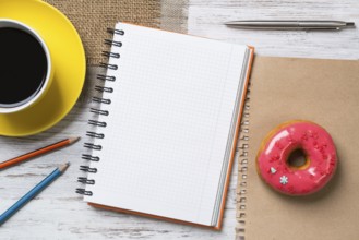 Opened notepad and cup of coffee with donut on wooden table